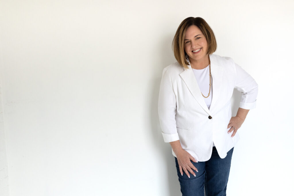 karen mcconomy woman standing against a white wall wearing blue jeans and a white blazer